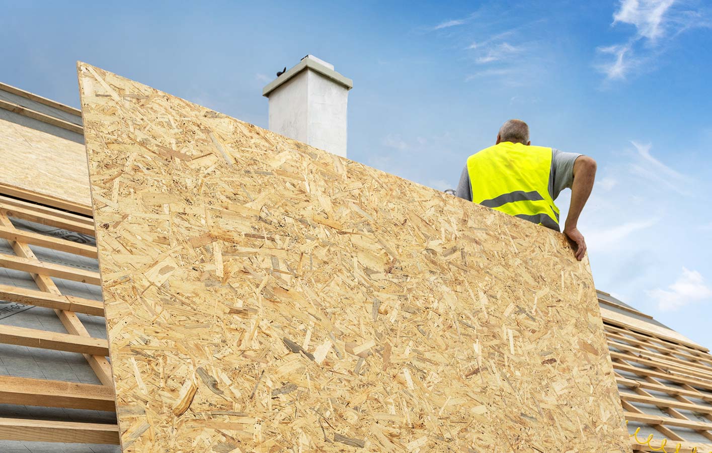 Mann auf Dach mit OSB-Platte in der Hand